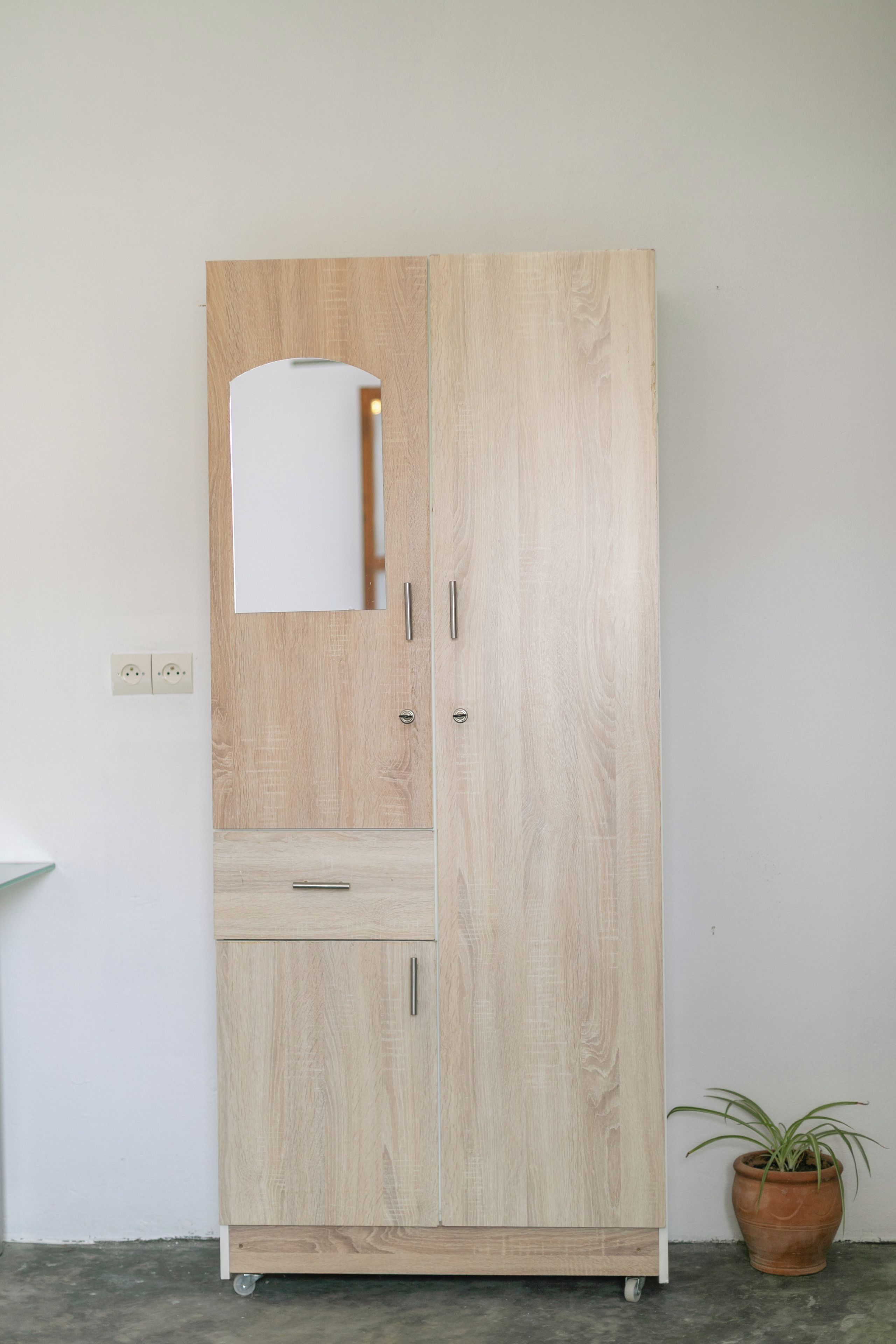 A tall wooden wardrobe with a mirror, a drawer, and a cabinet.