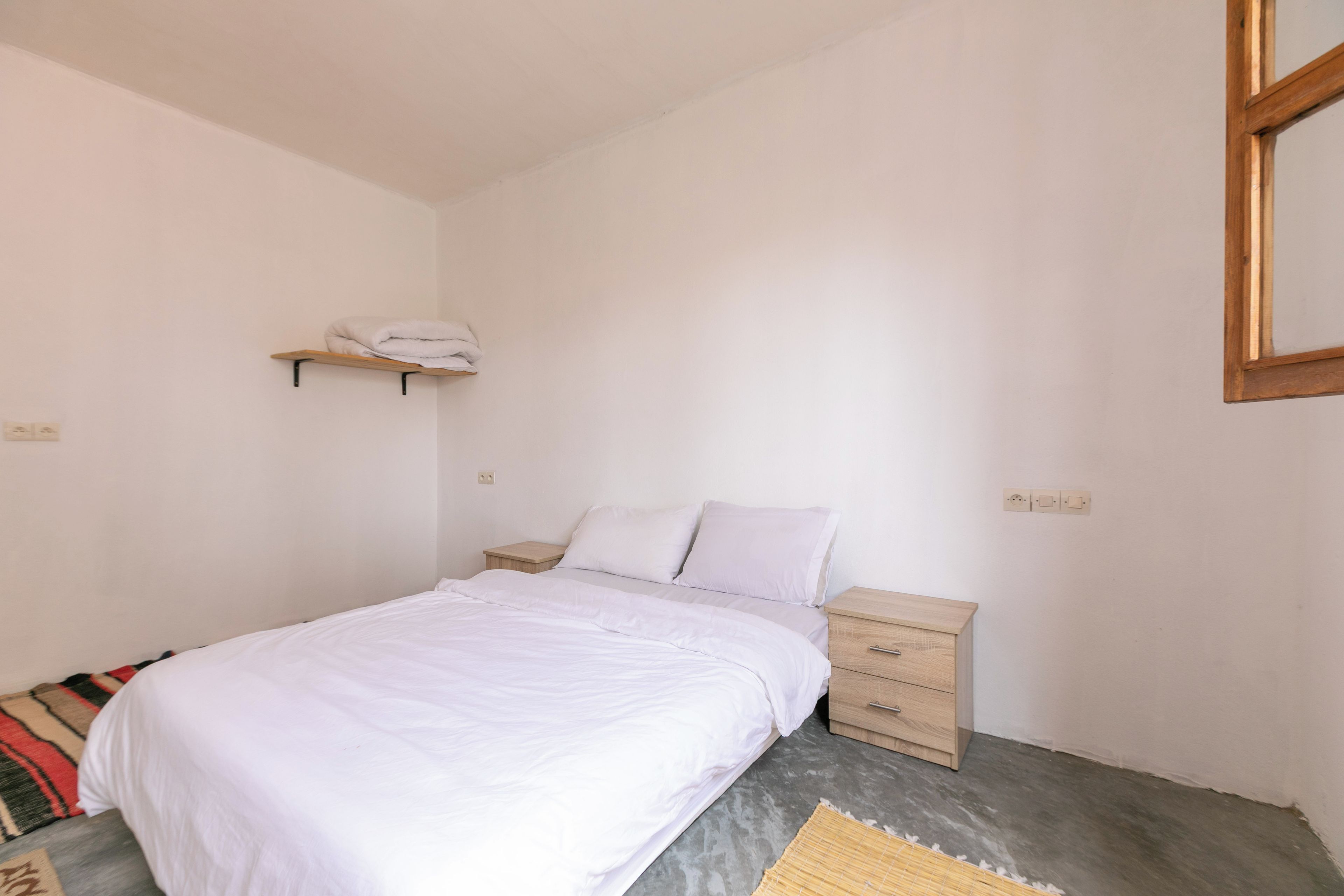Una camera da letto con un letto, un comodino, una mensola in legno e una presa a muro.
