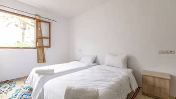 Un dormitorio con dos camas individuales, una mesita de noche de madera, un pequeño armario de madera y una ventana con cortinas.