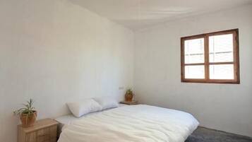 Un dormitorio con una cama, un ventanal, una lámpara y un tapete a rayas.