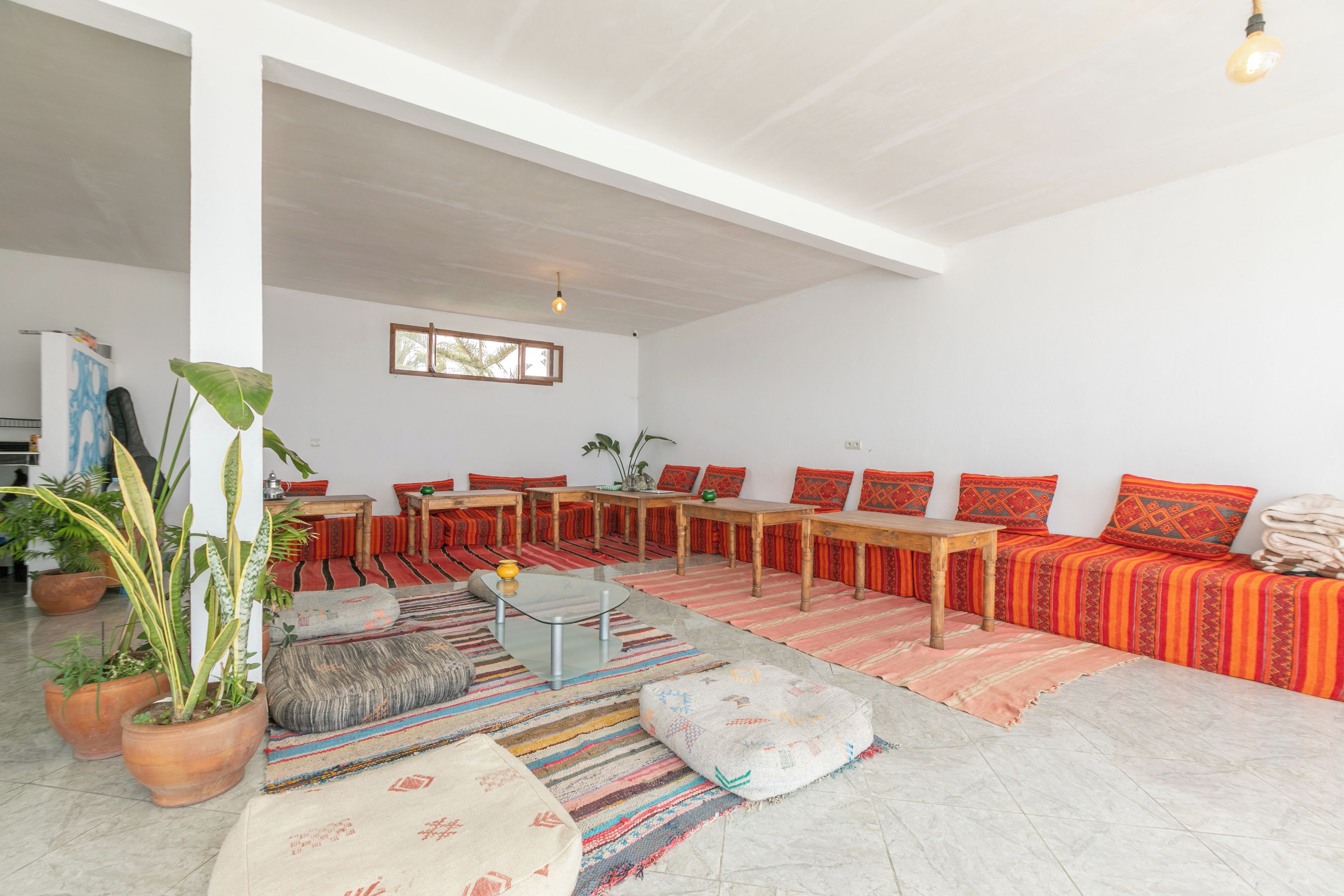 A spacious living area with a high ceiling, a long wooden sofa set, a glass coffee table, and a variety of colorful rugs.