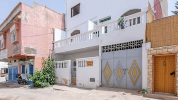 A two-story building with a balcony, a gated entrance, and a sign indicating it's a guesthouse.