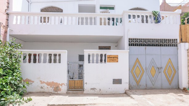 A two-story building with a balcony, a gate with a sign, and a decorative metal gate. - Hakuna Matata Guest House (TAMRAGHT)