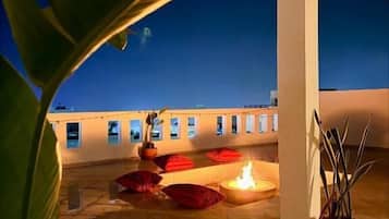 Una terraza en la azotea con una chimenea, plantas en macetas y vistas de la ciudad al anochecer.