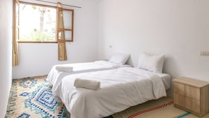 A room with two beds, a window with curtains, a hanging light fixture, and a patterned rug. - Hakuna Matata Guest House (TAMRAGHT)