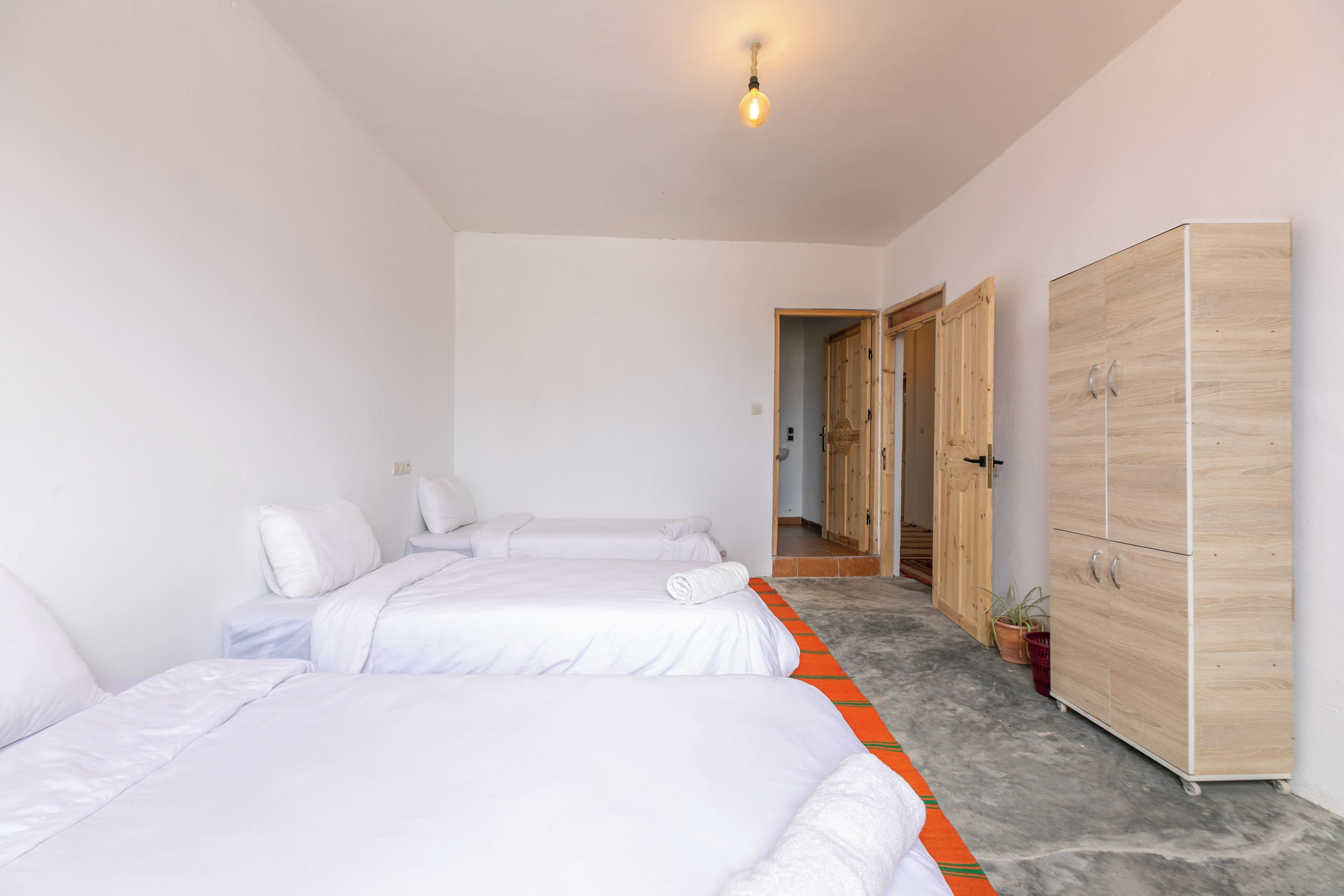 A hotel room with two beds, a wardrobe, and a hallway leading to another room.