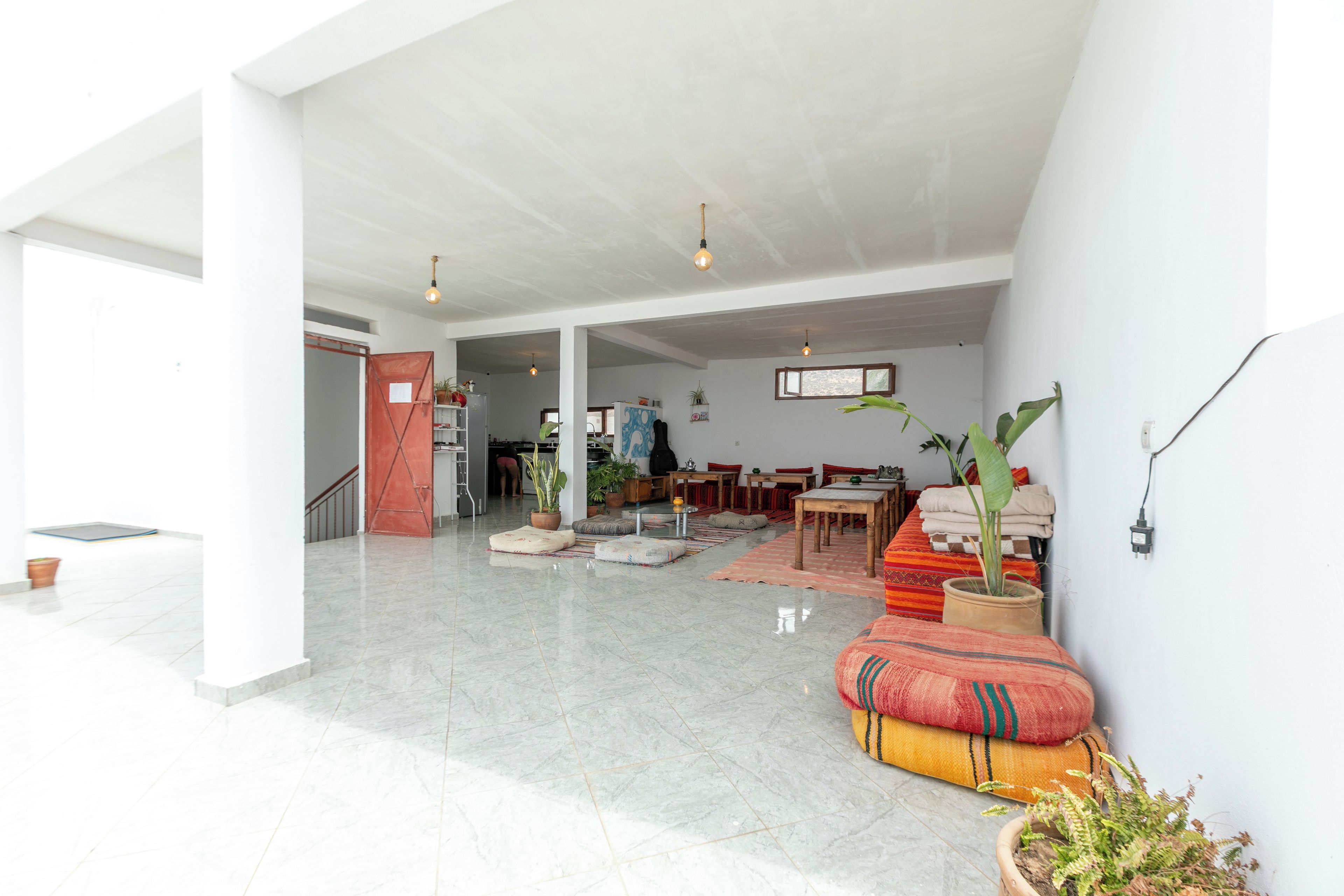A spacious living area with a high ceiling, a kitchen in the background, and a dining area with multiple tables.