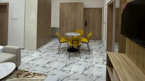 Una sala de estar moderna con suelo de mármol, una mesa redonda de comedor con sillas amarillas, un sofá, un televisor y paneles de madera en las paredes.