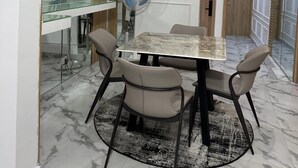 Un comedor moderno con una mesa de mármol, cuatro sillas, un tapete redondo y un ventilador de techo.
