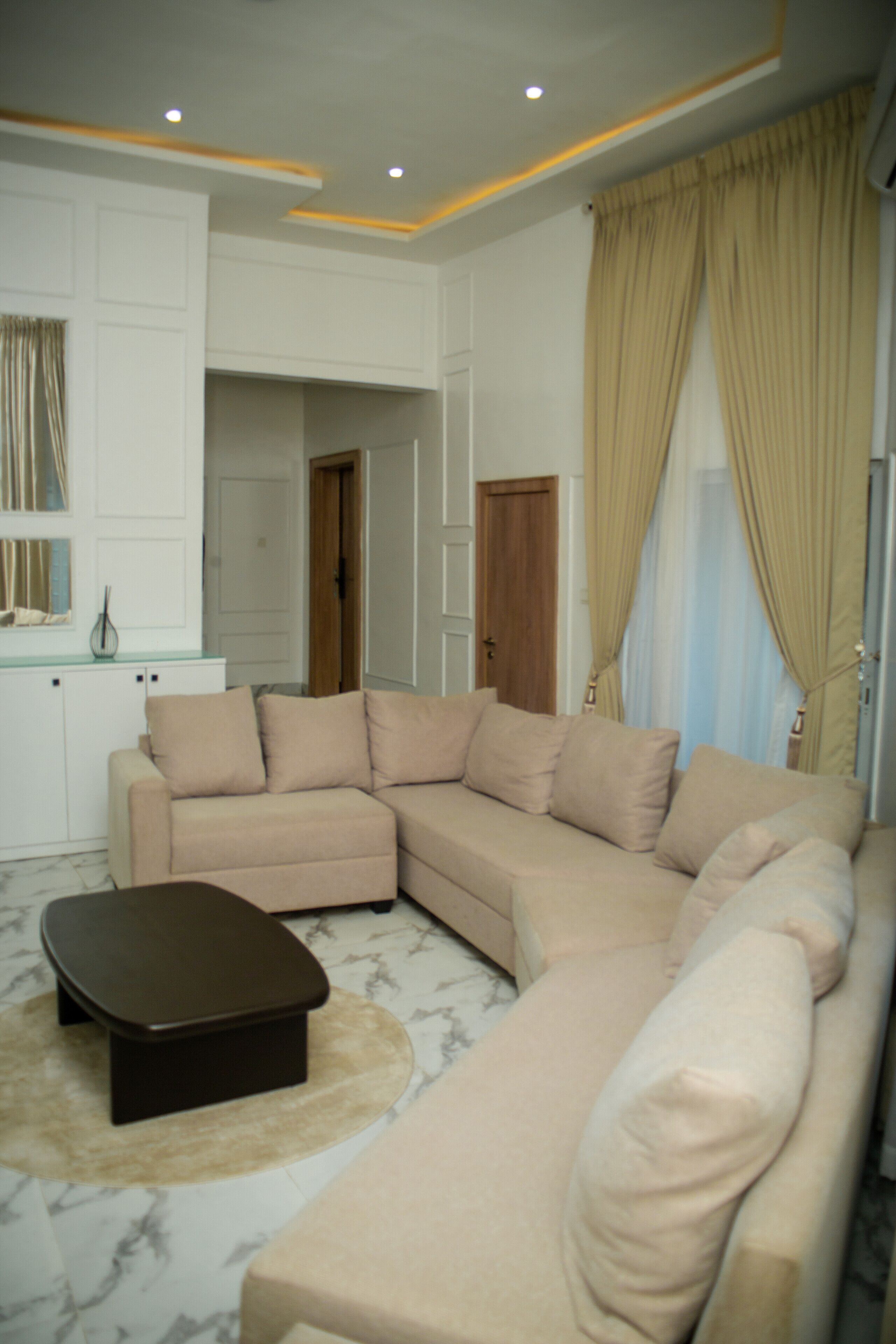 A living room with a beige sectional sofa, a small brown ottoman, and a white cabinet.