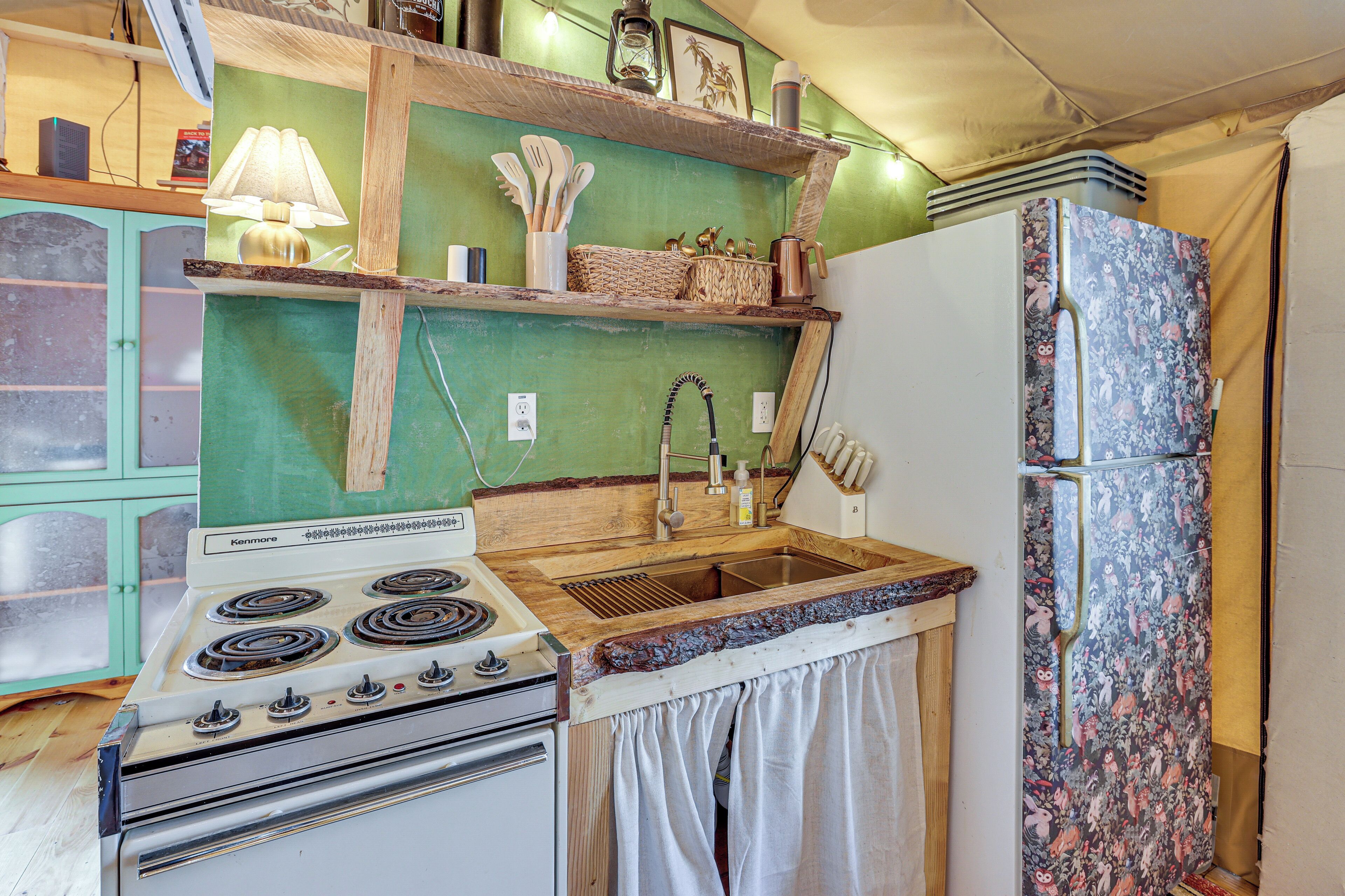 A compact kitchen with a Kenmore stove, wooden shelves, and a patterned refrigerator.
