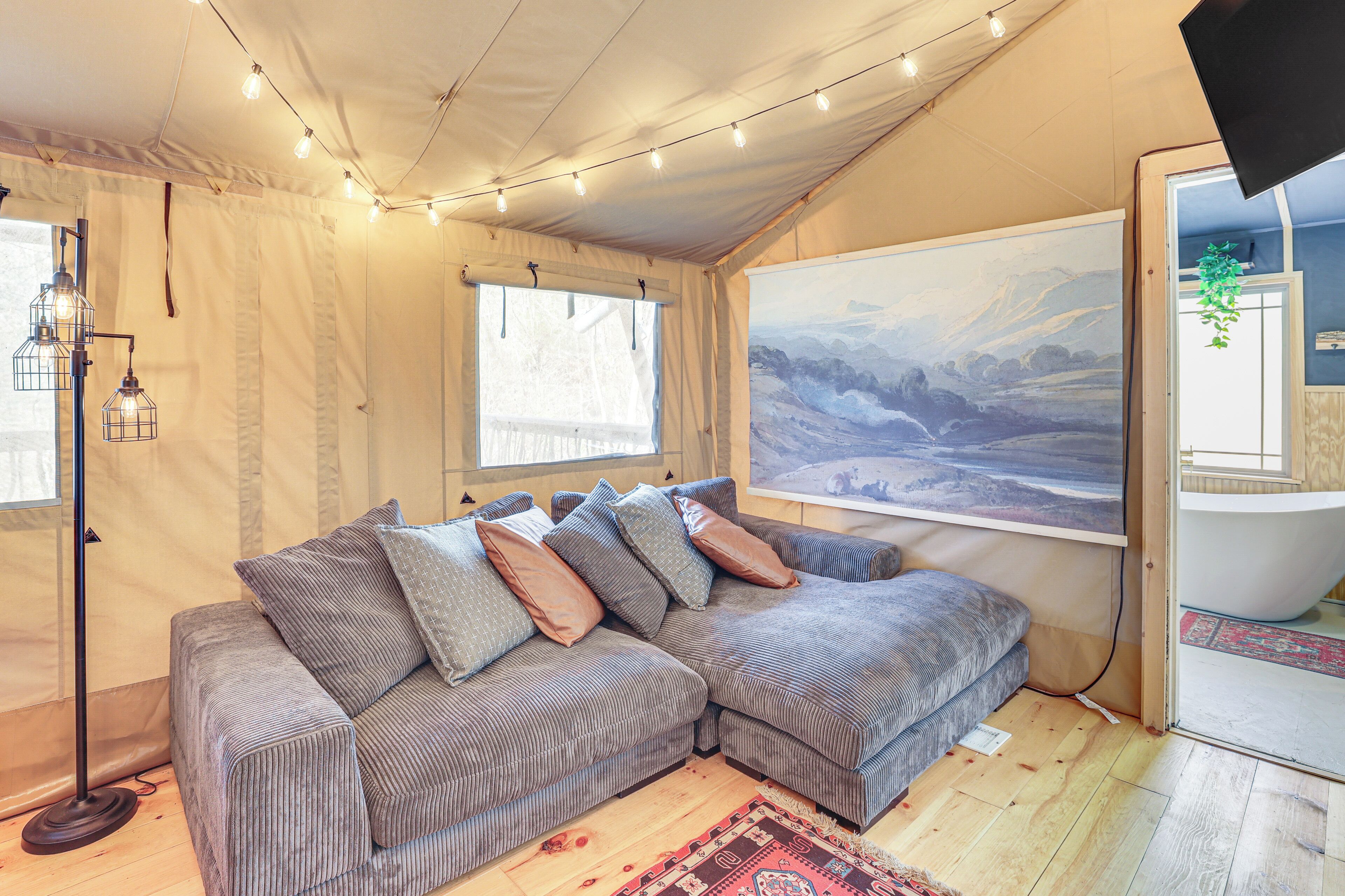 A cozy room with a large sectional sofa, a painting of a mountainous landscape, a hanging plant, and a visible door leading to another room.