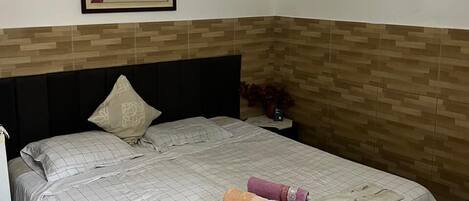 A bedroom with a bed, a nightstand, a wall clock, a framed picture, and a wall-mounted light fixture.