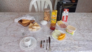 A table set with breakfast items including bread, pastries, fruit, and dairy products.