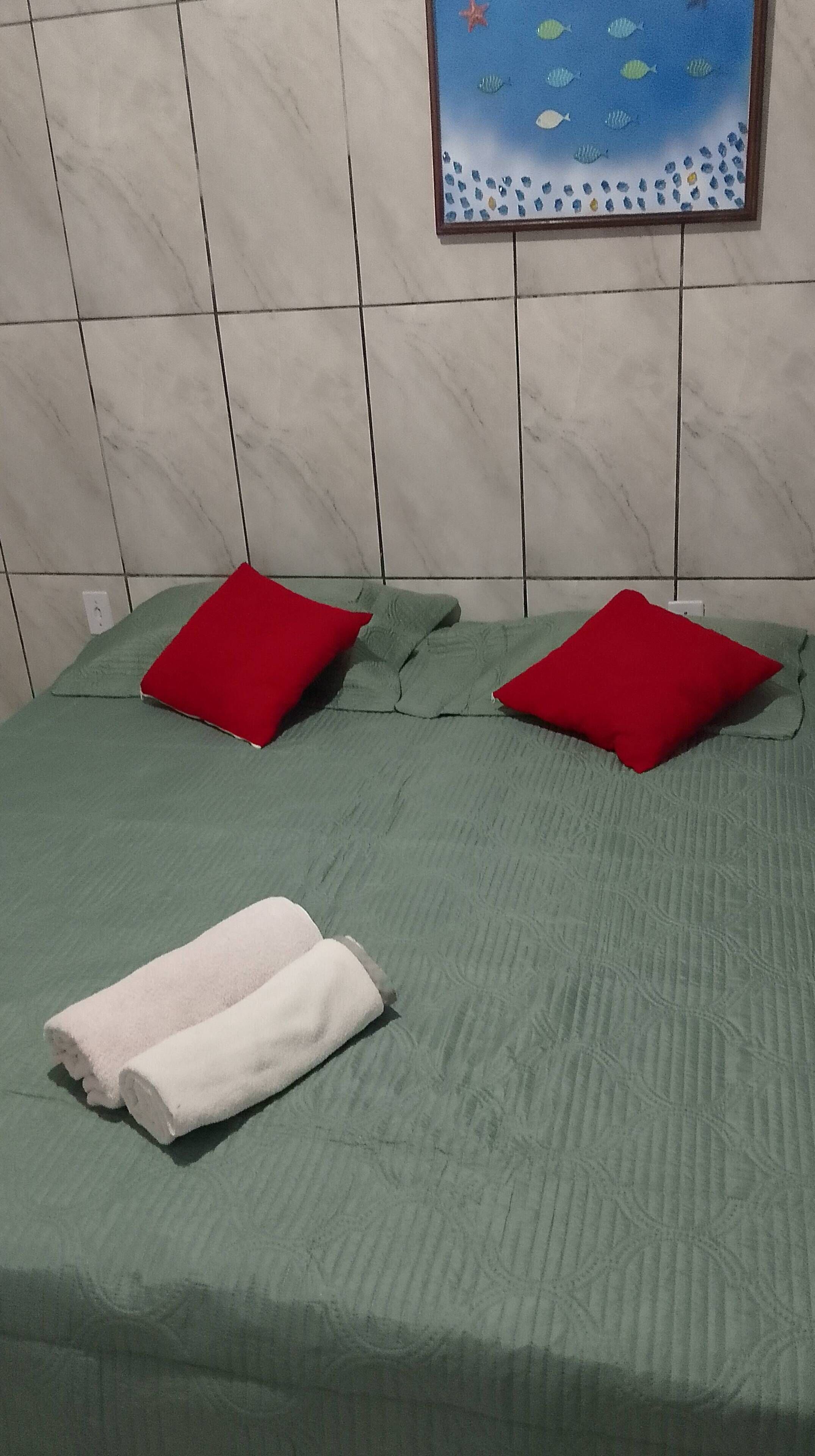 A bed with green bedding, two red pillows, and a white towel.