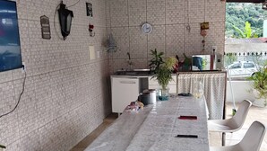 A covered outdoor dining area with a table, chairs, a small refrigerator, and a clock on the wall.