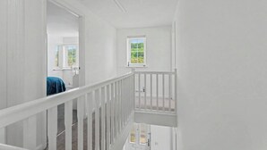 Un interior blanco con una escalera, una ventana con persianas y un ventilador de techo.