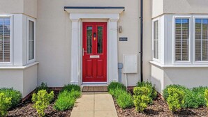 Una casa con puerta roja, detalles blancos y un pequeño jardín con setos podados.
