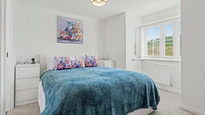 Un dormitorio con cama, paredes blancas, una ventana con persianas y un cuadro en la pared.