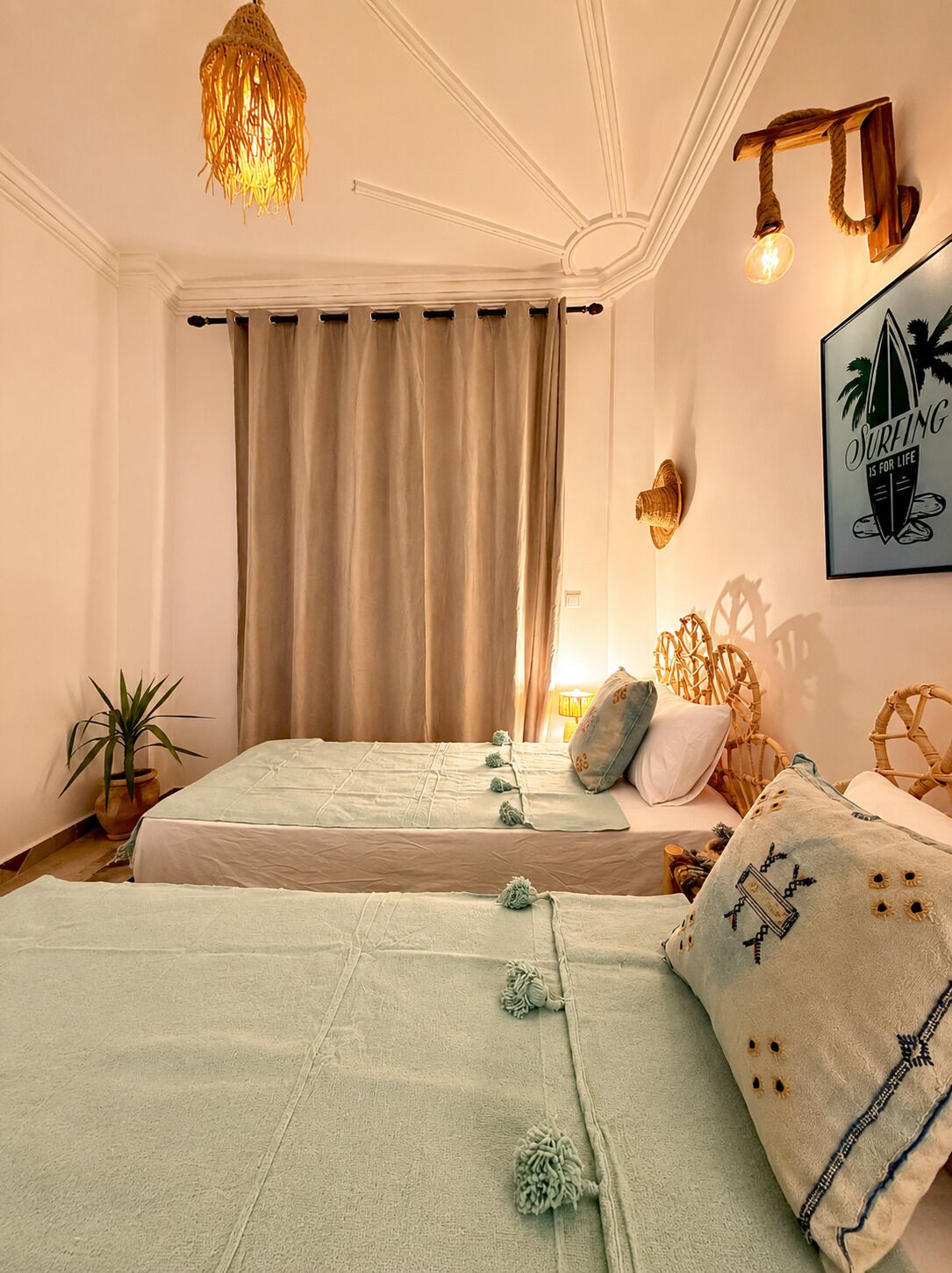 A room with two beds, a hanging light fixture, a wall-mounted light, and a framed picture.
