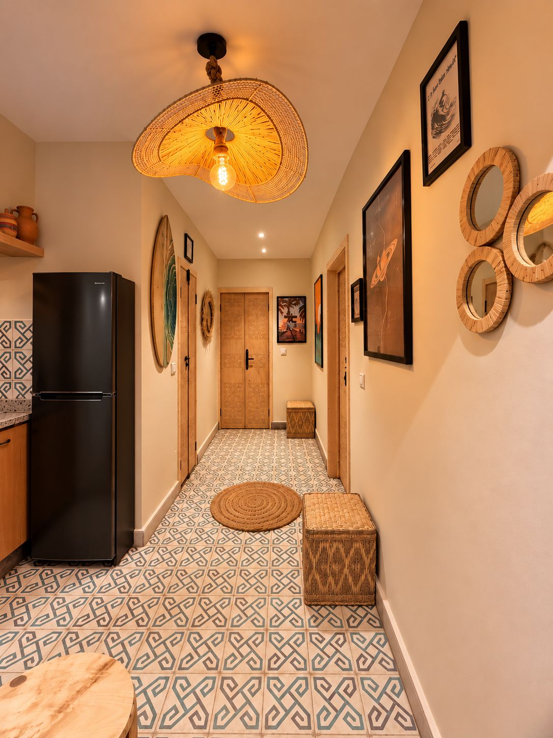 Un pasillo con baldosas de diseño, un refrigerador negro, una lámpara de fibra natural y espejos montados en la pared.