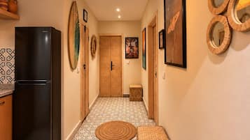 Un pasillo con baldosas de diseño, un refrigerador negro, una lámpara de fibra natural y espejos montados en la pared.