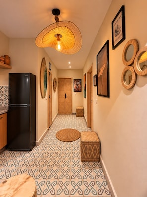 A hallway with patterned floor tiles, a black refrigerator, a woven light fixture, and wall-mounted mirrors. - Banana Surf Camp - Yoga Vibe and Retreat (Aourir)