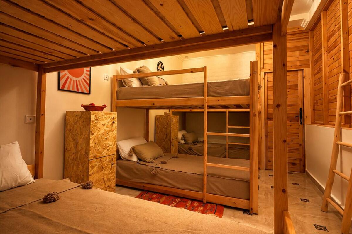 A wooden bunk bed room with a sloped ceiling, a stone accent wall, and a ladder.