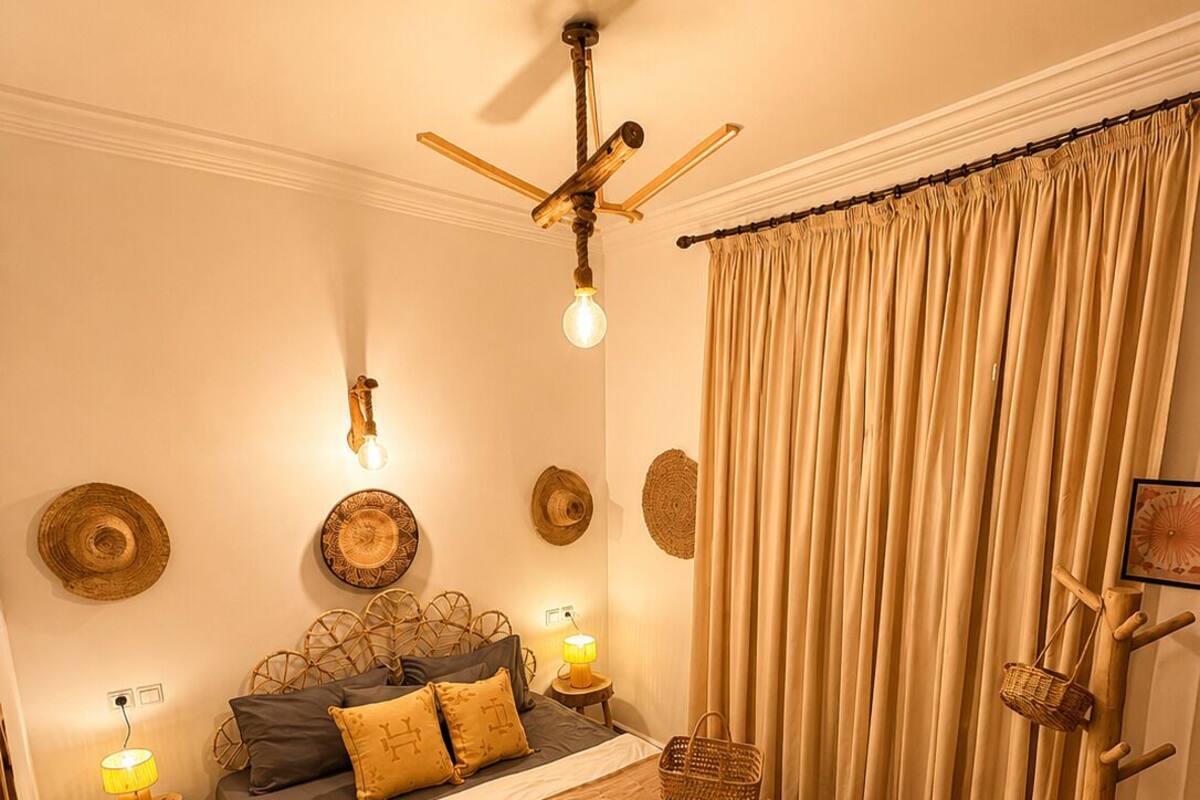 A bedroom with a bed, a ceiling fan, a bedside lamp, a wall-mounted shelf, and a large window with curtains.