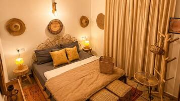 Een slaapkamer met een bed, een plafondventilator, een bedlampje, een wandplank en een groot raam met gordijnen.