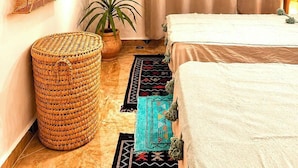 Un dormitorio con cama, cortinas, tapiz de pared tejido, planta en maceta, taburete tejido y alfombra estampada.
