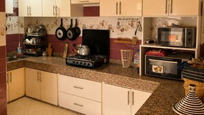 Una cocina con alacenas blancas, estufa a gas, microondas y un colgador para ollas.