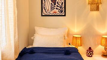 Un dormitorio con una cama, una ilustración enmarcadas de salvavidas, dos lámparas fijadas a la pared y un ventanal con cortinas.