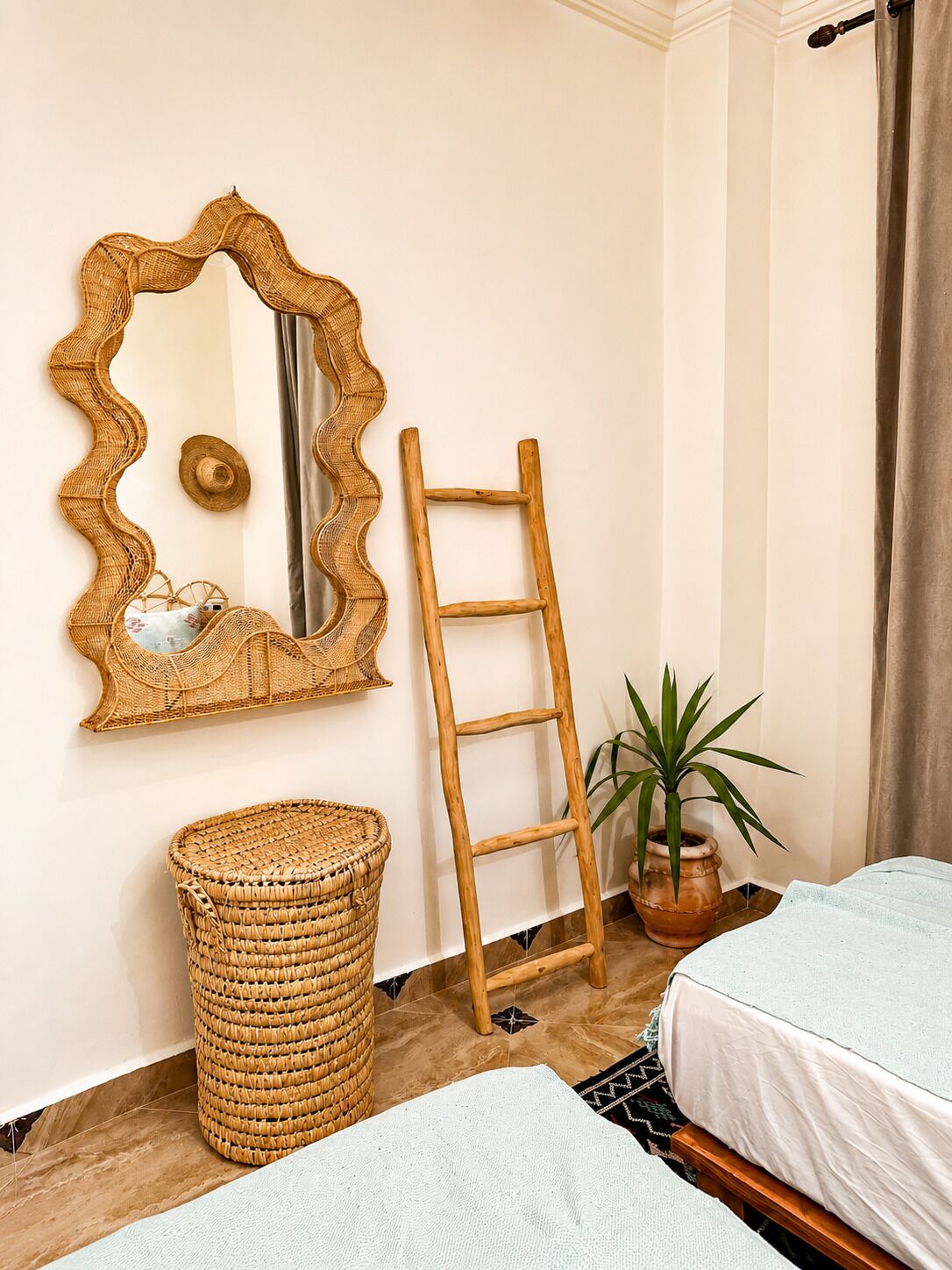 A room with a woven mirror, a wooden ladder, a wicker basket, a potted plant, and two beds.