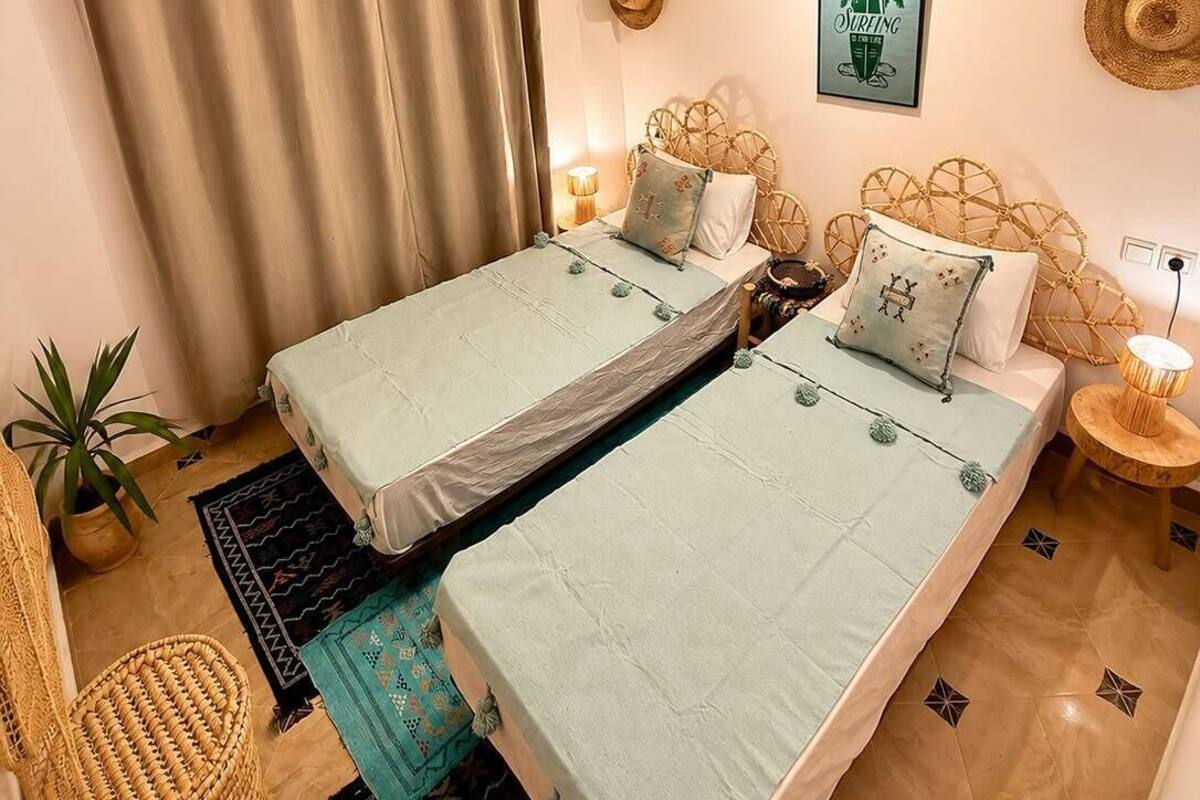 A bedroom with two beds, a hanging light fixture, a wall-mounted picture, and a woven basket.