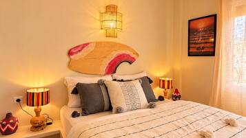 A bedroom with a large bed, two bedside lamps, a wall-mounted light fixture, a painting, and a window with curtains.