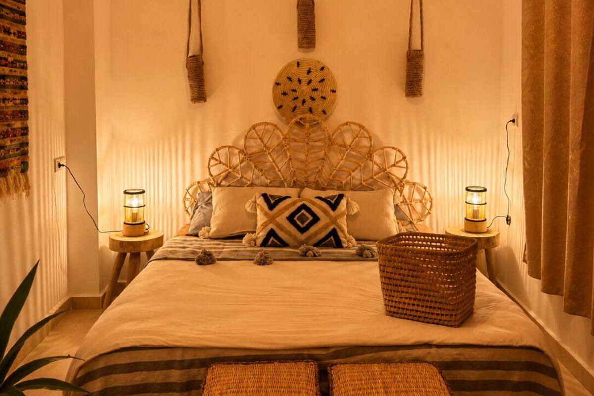 A cozy bedroom with a bed, two wall-mounted lamps, a woven headboard, and a large woven basket.