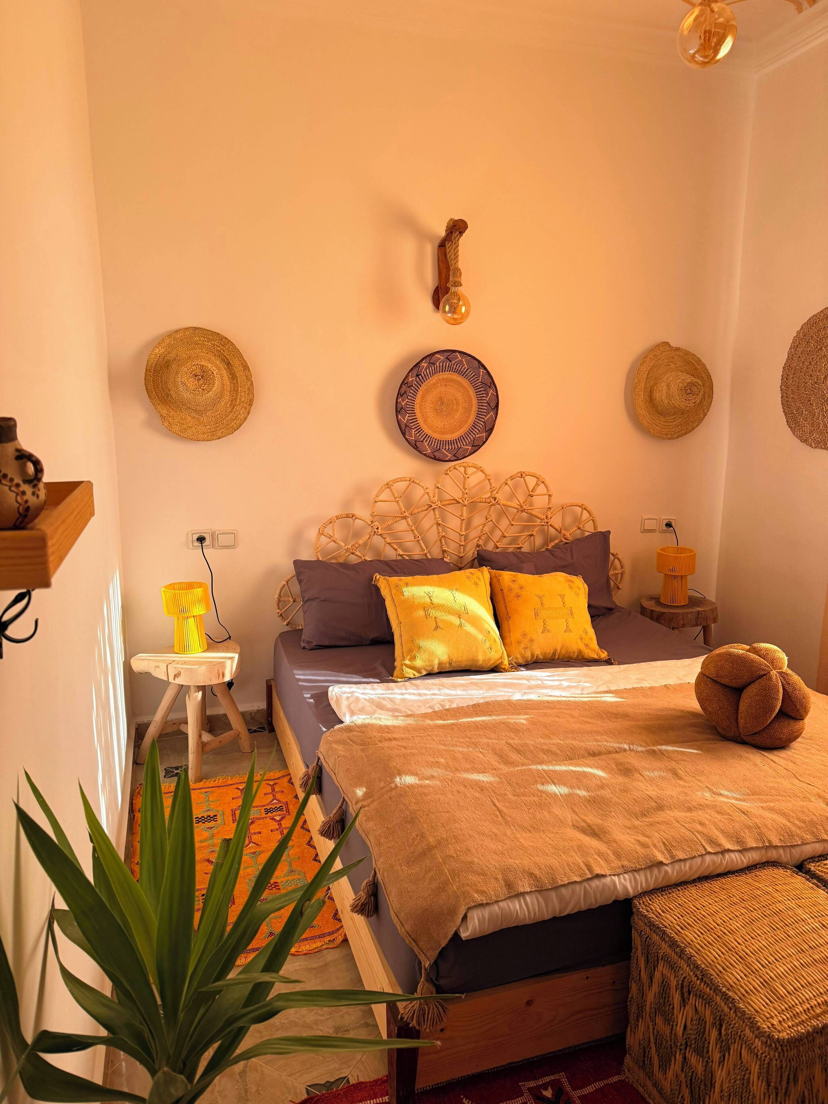 A bedroom with a bed, bedside lamps, a wall-mounted light fixture, and woven wall hangings.