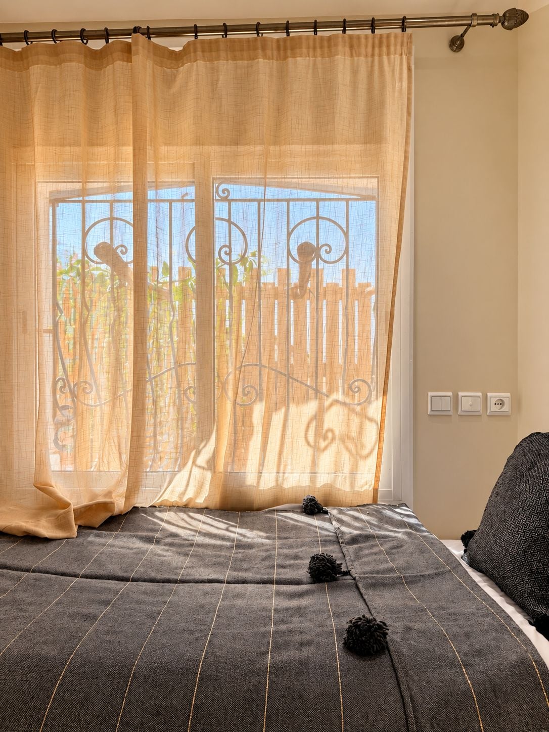 Een slaapkamer met een bed, een raam met uitzicht op een hek en een gordijn.