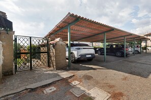 Un espace de stationnement couvert, doté d’un sol en gravier, d’une entrée fermée par un portail et d’un bâtiment avec un toit en tuiles.