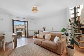 Un salon avec un canapé, une table à manger et des chaises, une plante en pot et une vue sur l’extérieur.