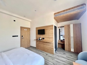 A modern hotel room with a bed, a TV mounted on a wooden panel, a wardrobe, and a mirror.