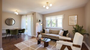 A living room with a sofa, a coffee table, a dining table with chairs, a large mirror, and a plant. - Oak & Earth Isle of Dogs Apartment (London)