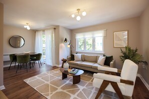 A living room with a sofa, a coffee table, a dining table with chairs, a large mirror, and a plant. - Oak & Earth Isle of Dogs Apartment (London)