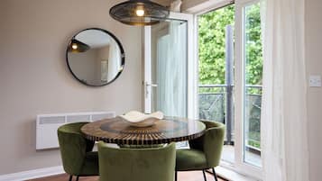 A dining area with a round table, two chairs, a hanging light fixture, a round mirror, and a sliding glass door leading to a balcony.