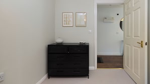A hallway with a black dresser, two framed pictures on the wall, and a white door. - Oak & Earth Isle of Dogs Apartment (London)