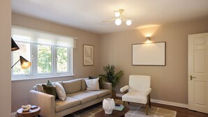 A living room with a sofa, armchair, coffee table, lamp, plant, and a framed picture on the wall. - Oak & Earth Isle of Dogs Apartment (London)
