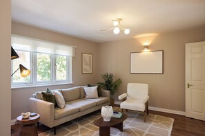 A living room with a sofa, armchair, coffee table, lamp, plant, and a framed picture on the wall. - Oak & Earth Isle of Dogs Apartment (London)