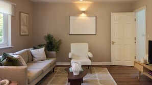 A living room with a sofa, armchair, coffee table, and a framed picture on the wall. - Oak & Earth Isle of Dogs Apartment (London)