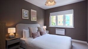 A bedroom with a bed, bedside tables, wall art, a window, and a ceiling light fixture. - Oak & Earth Isle of Dogs Apartment (London)